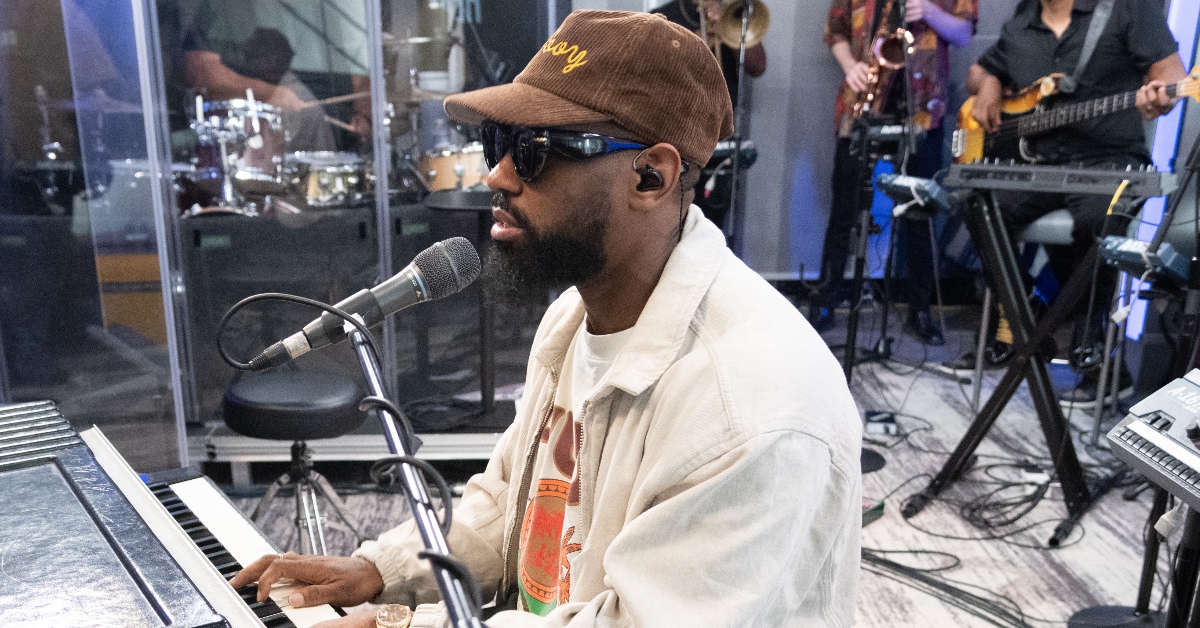 PJ Morton sings into a microphone and plays the keyboard during a live session.