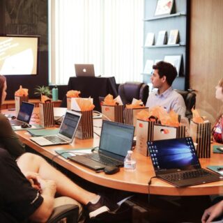 Employees collaborate around a table with gift bags and digital devices, showcasing RFP management for improving proposal workflow and teamwork