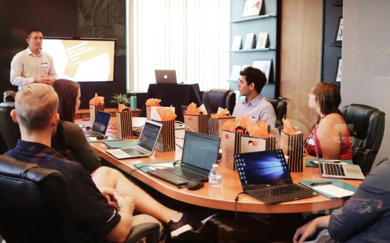Employees collaborate around a table with gift bags and digital devices, showcasing RFP management for improving proposal workflow and teamwork